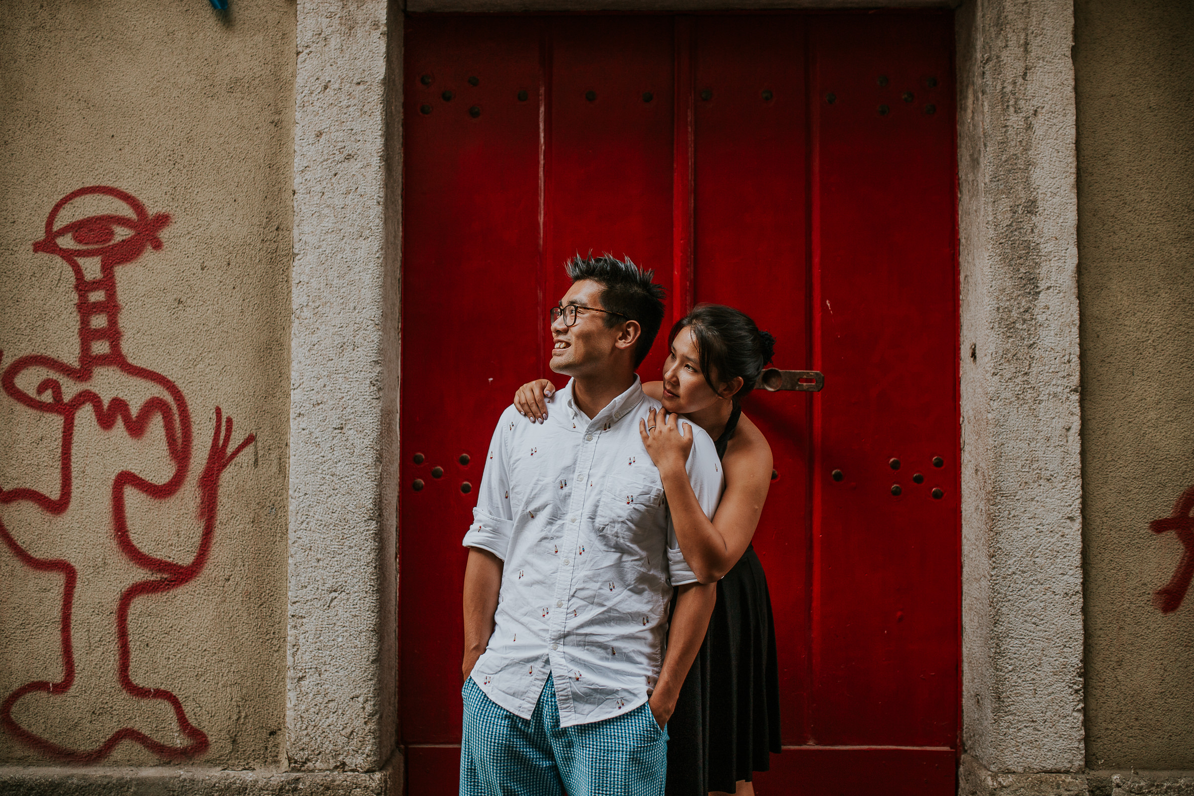 asian couple embraced with a red door as background in lisbon
