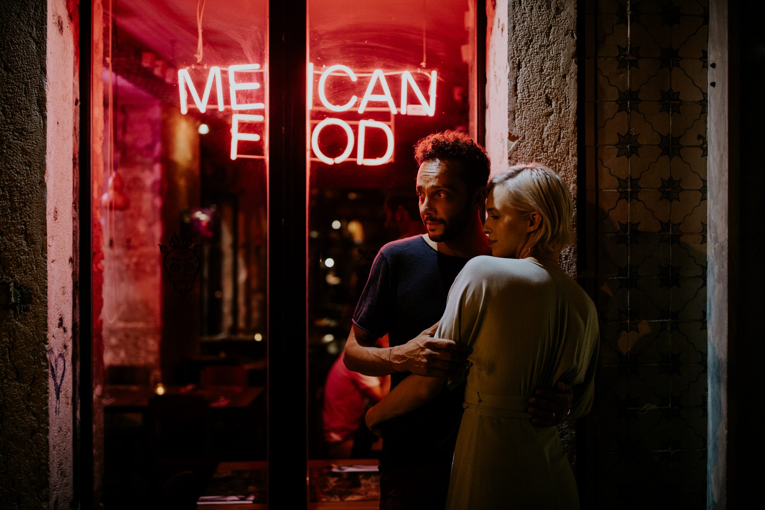 couple embracing at night next to a mexican food restaurant with red neons