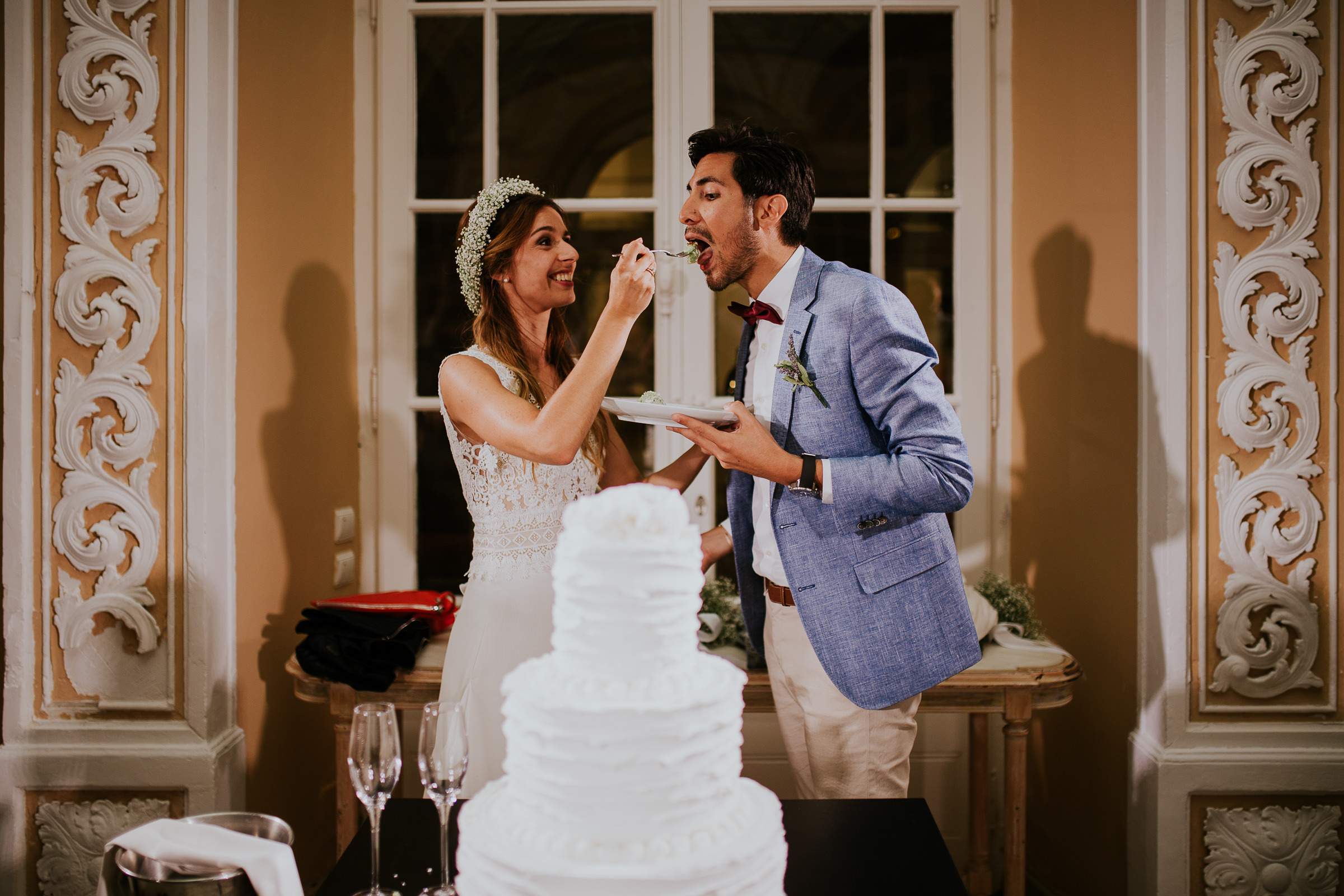 Funny bride feeding his groom with a piece od wedding cake
