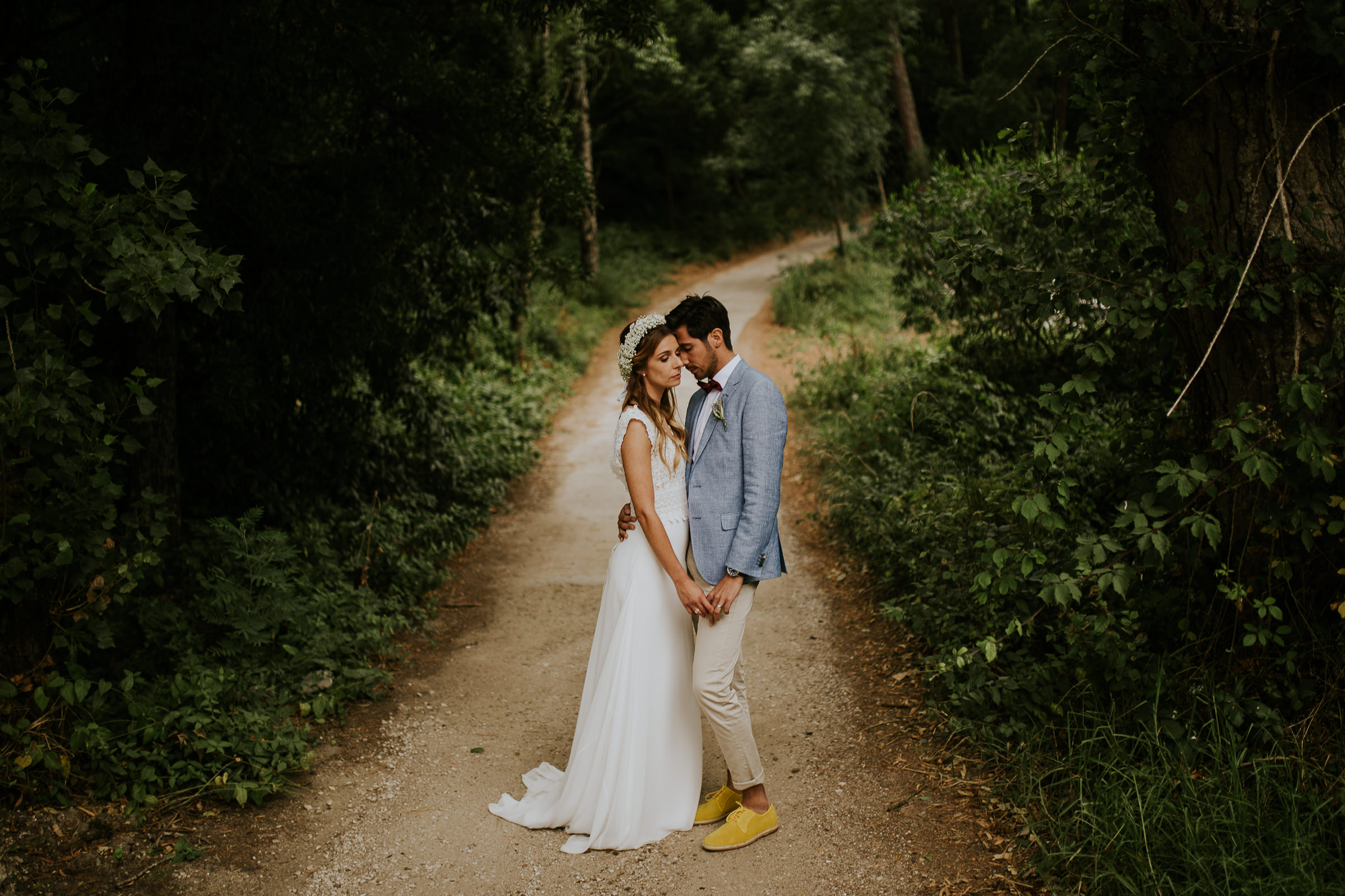 Centered posed portrait of bride and groom on a path in the middle of woods